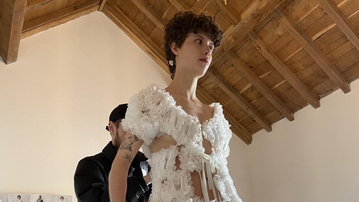 a model gets fitted with a very transparent white wedding gown made of big ruffles over white underwear