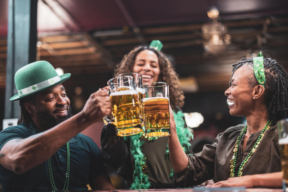 Three people celebrating, wearing St. Patrick's Day accessories, toasting with beer