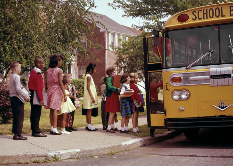 Children in vintage attire line up to board a school bus