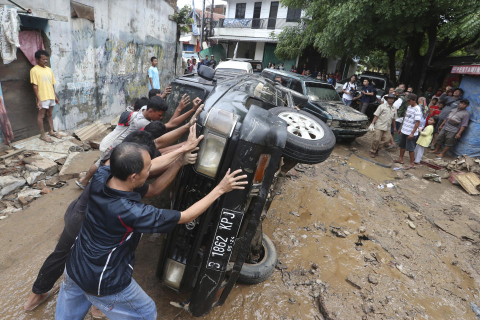 Residents move the wreckage of cars that were swept away by flood in Bekasi, West Java, Indonesia, Friday, Jan. 3, 2020. Severe flooding in greater Jakarta has killed scores of people and displaced tens of thousands others, the country's disaster management agency said. (AP Photo/Achmad Ibrahim)