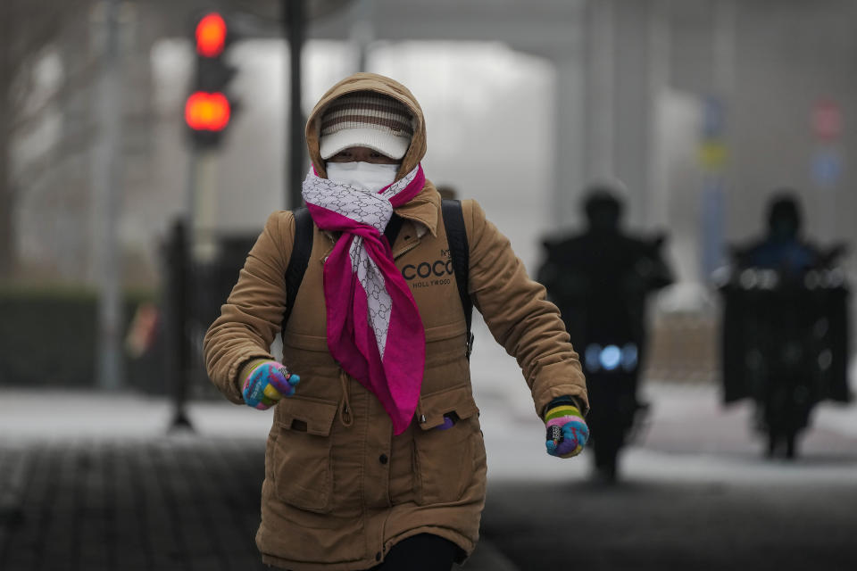 A woman wearing a face mask and covered with hood runs across a street Beijing, Monday, Dec. 12, 2022, as the capital city is hit by sandstorm. China will drop a travel tracing requirement as part of an uncertain exit from its strict "zero-COVID" policies that have elicited widespread dissatisfaction. (AP Photo/Andy Wong)