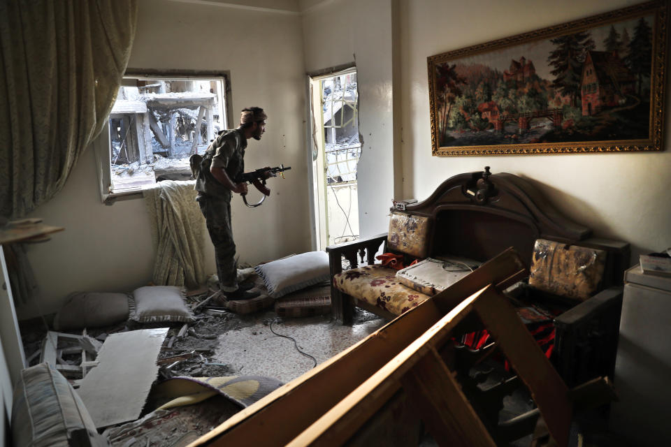 FILE - In this Thursday, July 27, 2017 file photo, a U.S.-backed Syrian Democratic Forces fighter, looks through a window as he takes his position inside a destroyed apartment on the front line, in Raqqa city, northeast Syria. With Islamic State's near total defeat on the battle field, the extremist group has reverted to what it was before its spectacular series of conquests in 2014 _ a shadowy terror network that targets vulnerable civilian populations and exploits state weaknesses to incite on sectarian strife. But a recent surge in false claims of responsibility for attacks also signals that the group is struggling to stay relevant after losing its proto-state and its dominance of the international news agenda. (AP Photo/Hussein Malla, File)