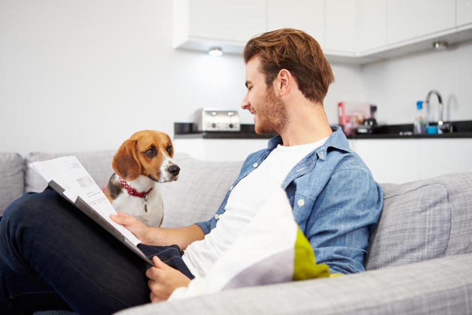 A man reads a newspaper while a dog sits on the couch next to him. 