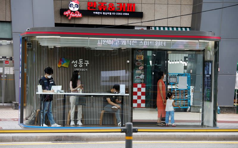 People wait for a bus inside a glass covered stop in Seoul