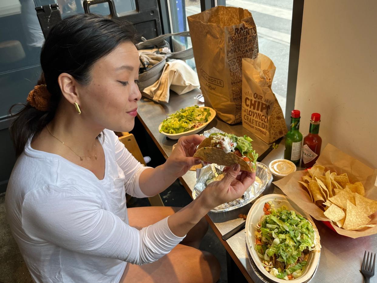 tiffany holding a taco from chipotle in front of a table of chipotle food