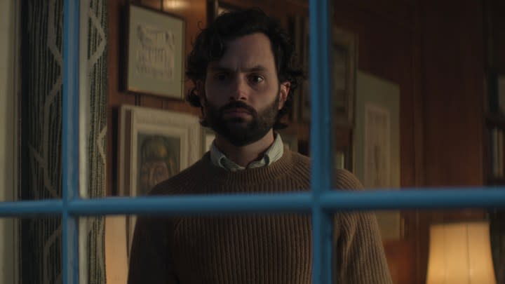 Joe Goldberg standing behind a barred window in a scene from You season 4.