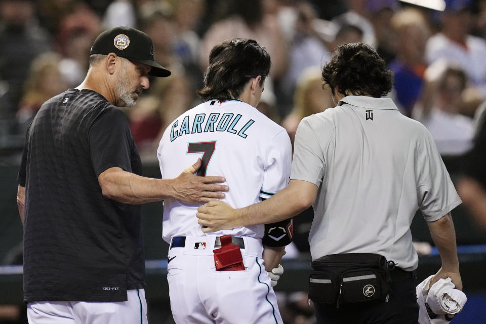 Arizona Diamondbacks' Corbin Carroll, middle, is helped off the field by manager Torey Lovullo, left, and a member of the training staff after Carroll injured his shoulder while batting during the seventh inning of the team's baseball game against the New York Mets on Thursday, July 6, 2023, in Phoenix. (AP Photo/Ross D. Franklin)