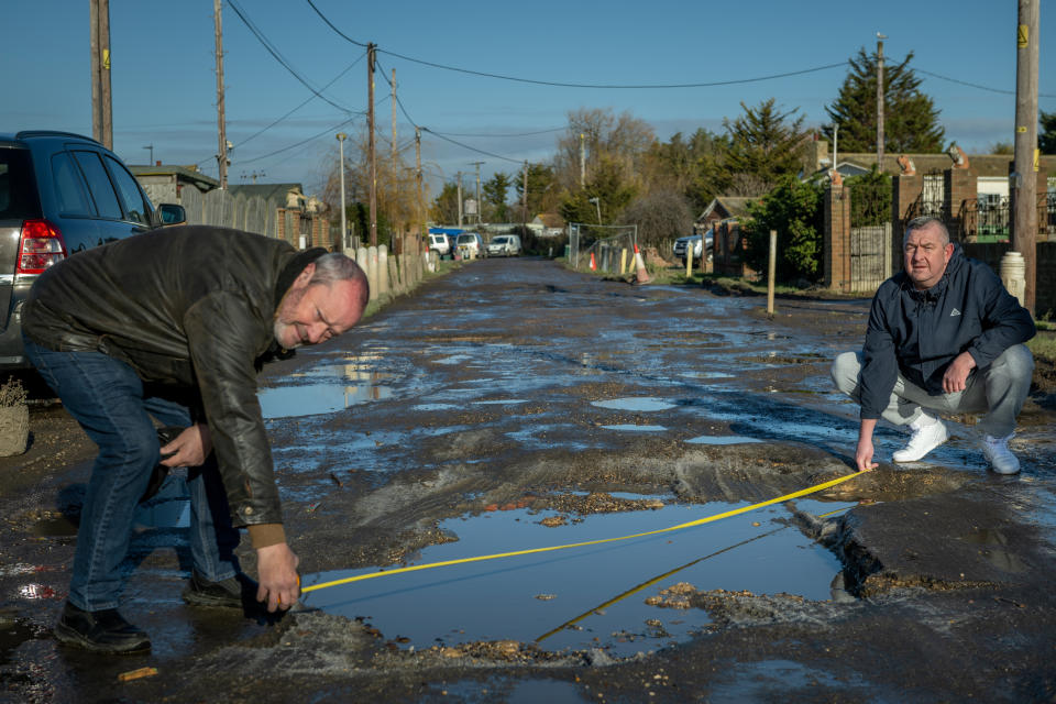 Two residents measure one of the potholes. (SWNS)