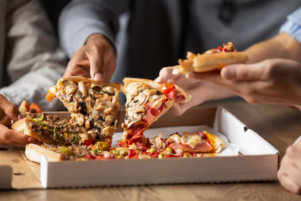 Primer plano de jóvenes multirraciales reunidos en una pizzería disfrutando de compartir deliciosa comida italiana, diversos colegas o amigos tomando porciones de pizza y disfrutando de comida de bar, servicio de entrega para llevar