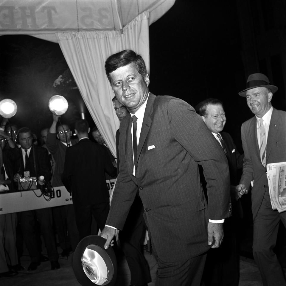 President Kennedy, hat in hand, leans slightly forward as he glances at bystanders upon his arrival at the Carlyle Hotel here September 19th.  The Chief Executive is scheduled to address the 18th session of the United Nations General Assembly September 20th.  He is expected to discuss the partial nuclear test ban treaty and prospects for further reductions in East-West tensions.