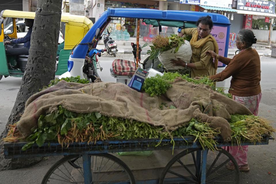Preethi, left, a 38-year-old transgender woman who uses only her first name, hands over a sack of vegetables to her customer who traveled in her electric auto rickshaw in Bengaluru, India, Monday, July 10, 2023. She's now one of millions of electric vehicle owners in India, but one of very few to have received an EV through a charitable donation. (AP Photo/Aijaz Rahi)