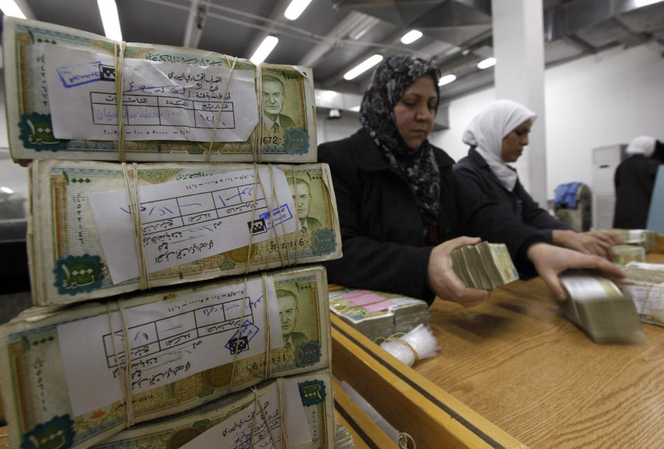 FILE - In this January 13, 2010 file photo, Syrian employees stack packets of Syrian currency in the Central Syrian Bank in, Damascus, Syria. With Syria's currency hitting record lows, a nationwide symbolic campaign has been launched by merchants, barbers, supermarkets and even gyms to support the Syrian pound. (AP Photo/Hussein Malla, File)