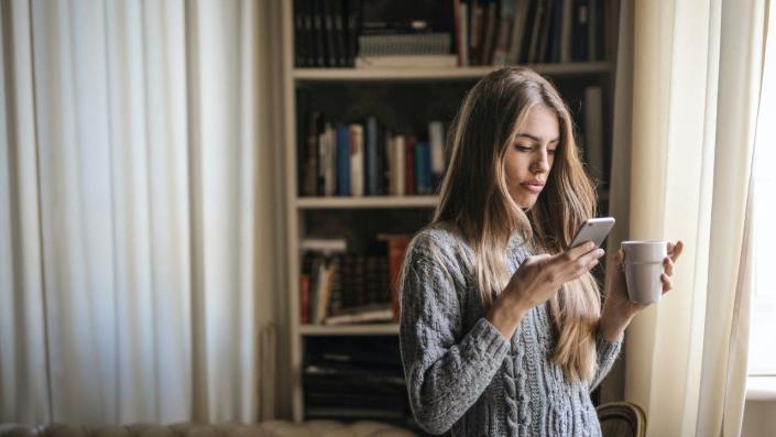 Woman sits in bedroom while texting on her phone