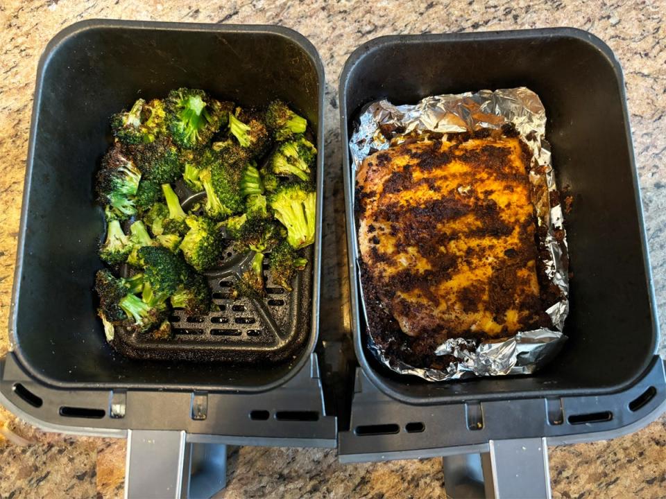 The two baskets of the Ninja DualZone Air Fryer, holding coked broccoli in one and a chicken breast in the other.