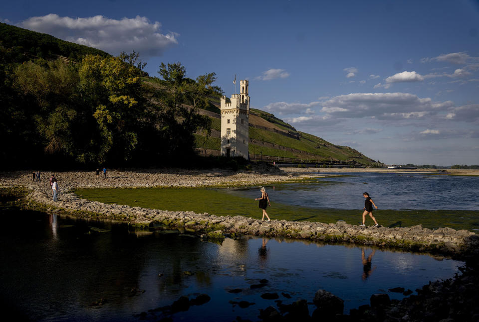 People walk over a stone dam, that is normally covered by water, towards the "Maeuseturm" (mice tower) in the middle of the river Rhine in Bingen, Germany, Friday, Aug. 12, 2022. The Rhine carries low water after a long drought period. (AP Photo/Michael Probst)