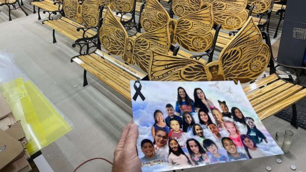 PHOTO: Sean Peacock holds a photo of the 21 victims of the Robb Elementary School shooting in front of the memorial benches he made in their honor. (Sean Peacock)