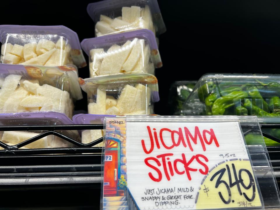 Several boxes of precut jicama sticks next to clear containers of peppers on a shelf at Trader Joe's. A sign reads "Jicama sticks $3.49" in the foreground