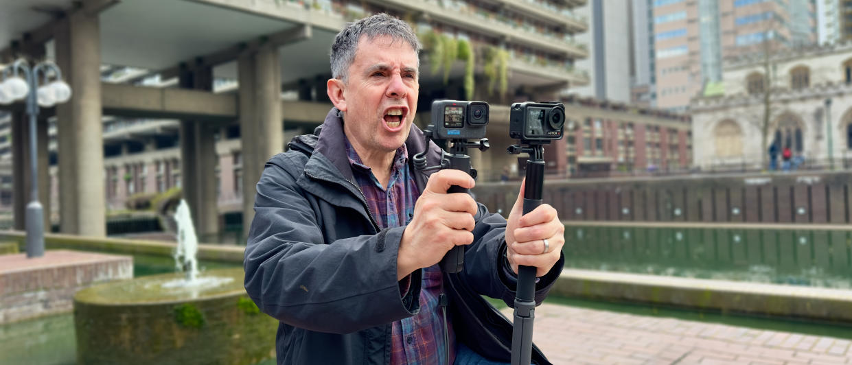  A man holding up two action cameras next to each other and yelling. 