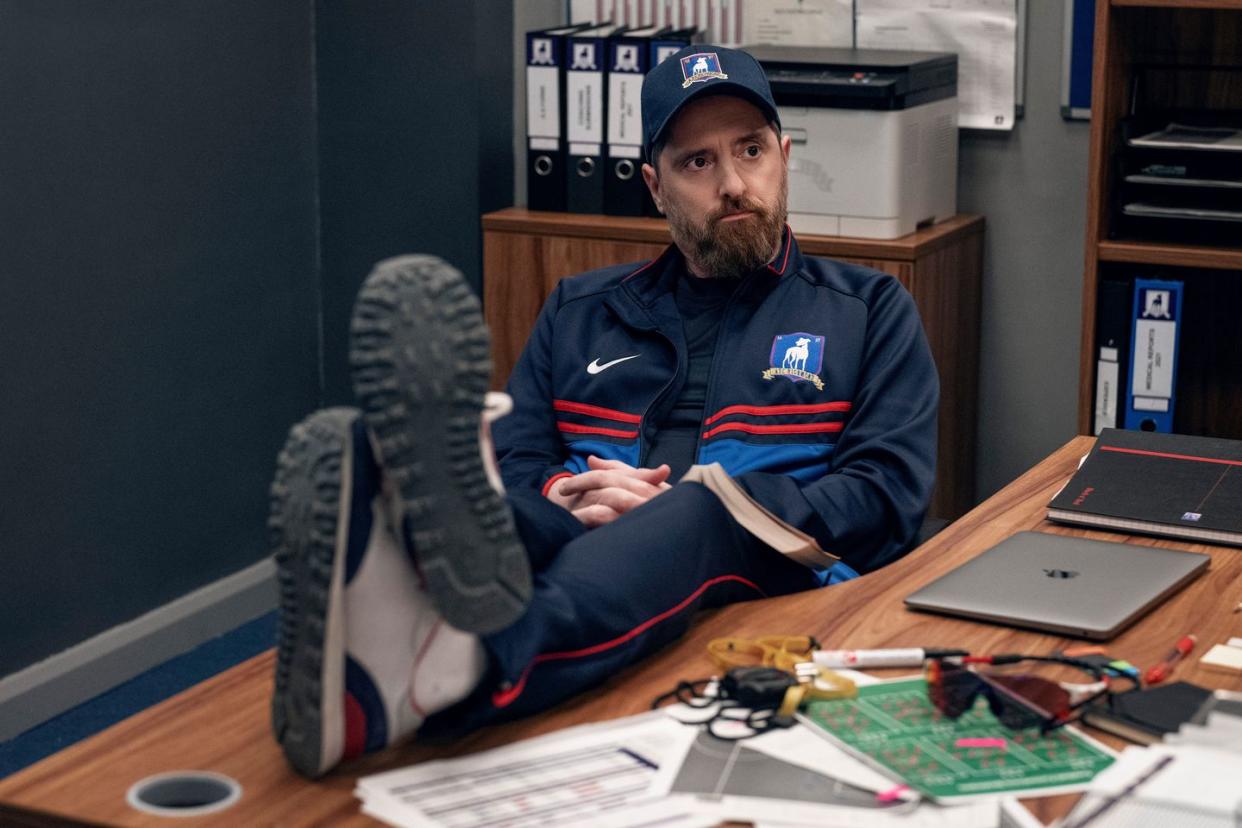 in a scene from ted lasso season 3, coach beard sits with his feet up on the desk in the team office