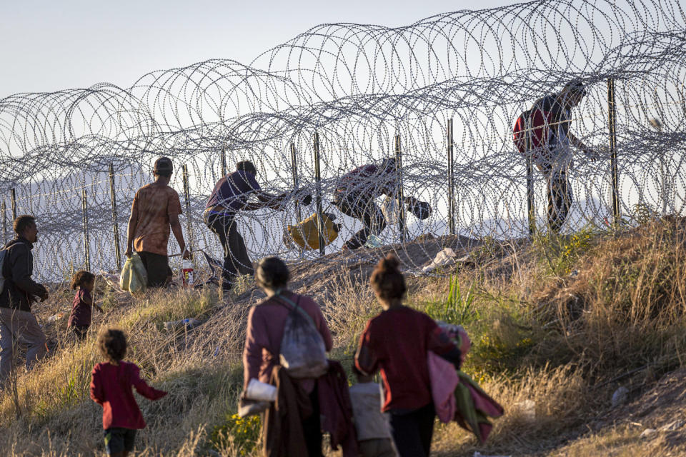 Migrants cross through a barbed-wire fence. (John Moore / Getty Images)