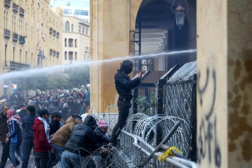 An anti-government protester gestures as security forces spray water cannon at demonstrators during clashes in the downtown district of the Lebanese capital Beirut