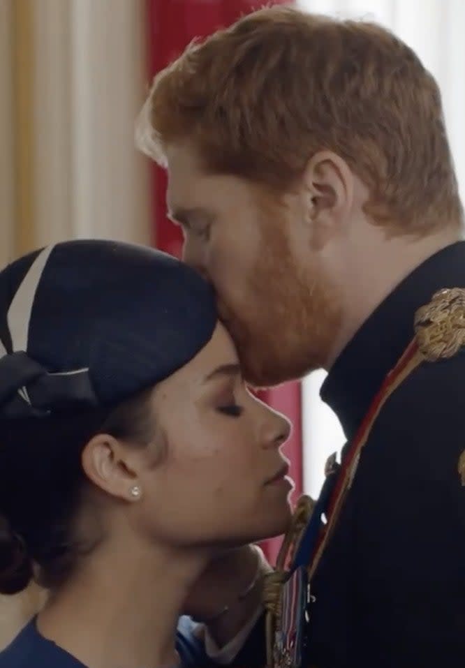 A screenshot from the movie where Harry kisses Meghan's head