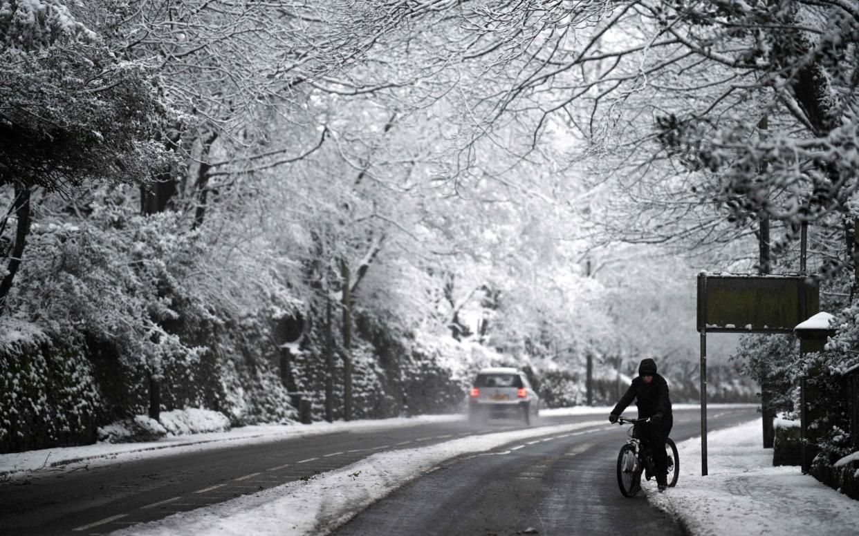 A cyclist makes their way along a snow covered road in Marsden - AFP