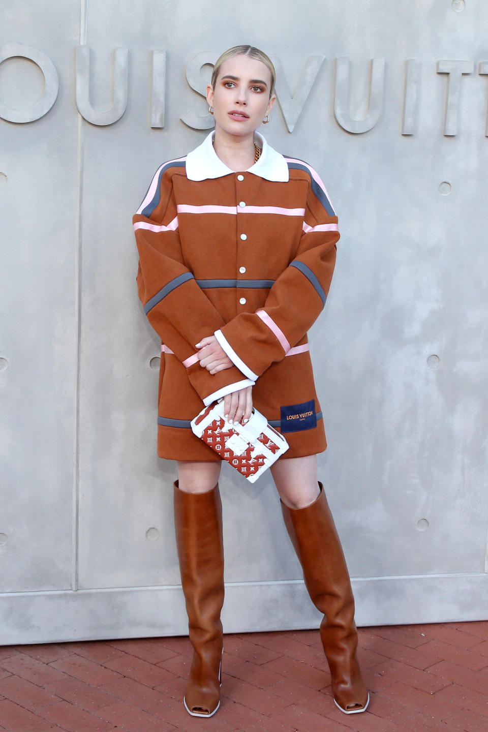 Emma poses for photographers at a Louis Vuitton event while wearing a Louis coat, knee-high boots with an open toe and a Louis purse