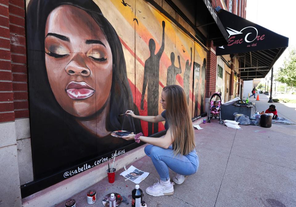 Isabella Siebert paints highlights on a mural of Breonna Taylor on boards covering the windows at Encore on S. 4th Street in Louisville, Ky. on Oct. 13, 2020.  Artists have been transforming the boards into art to be auctioned off and removed from downtown businesses.
