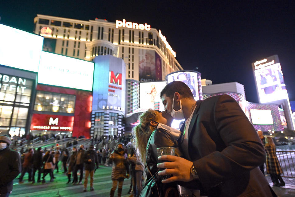 FILE - In this Dec 31, 2020, file photo, a couple kiss as they celebrate New Year's Eve along the Las Vegas Strip in Las Vegas. Thousands of New Year’s revelers gathered beneath the neon-lit marquees on the Las Vegas Strip — even though the big annual fireworks show was called off due to the coronavirus pandemic. (AP Photo/David Becker, File)