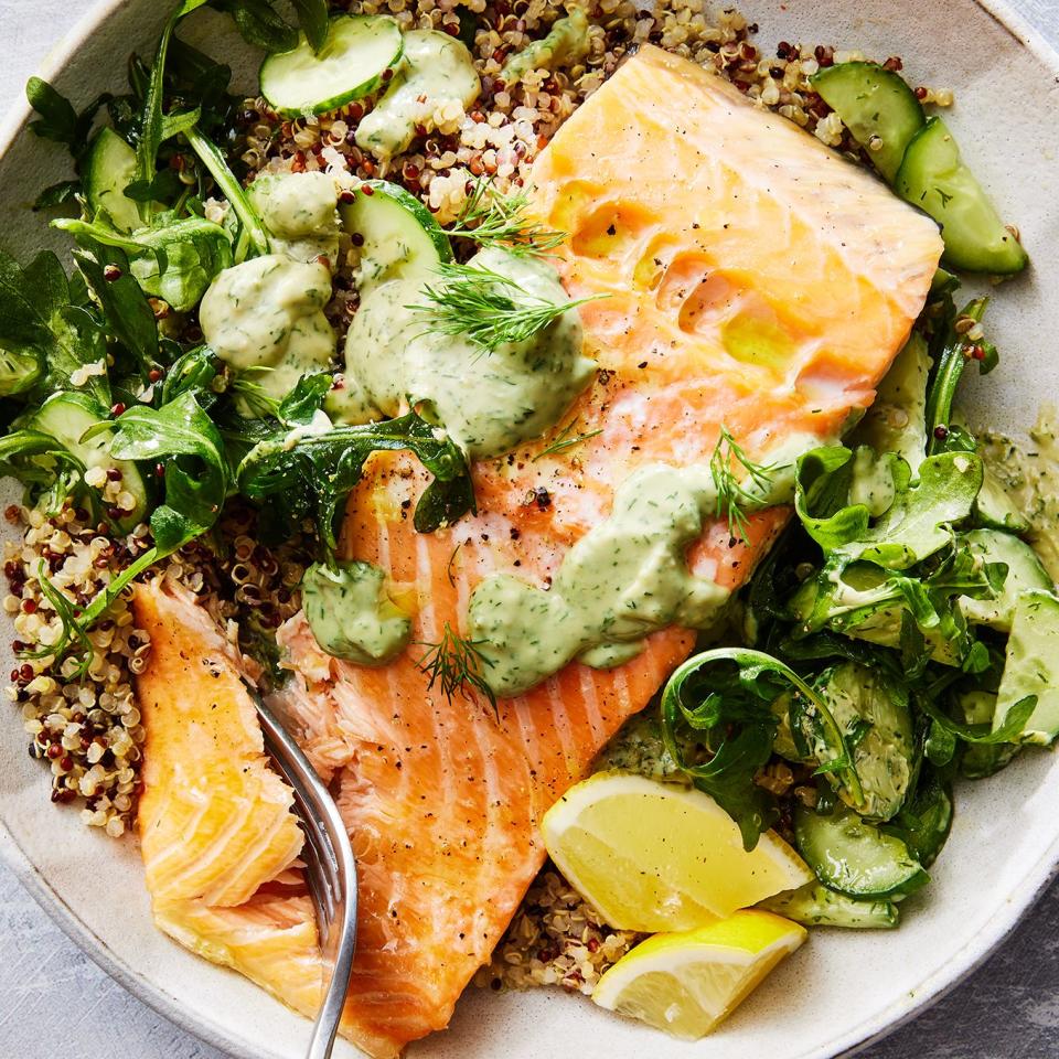 quinoa in a bowl with salmon, arugula, cucumber, lemon wedges, and a green sauce