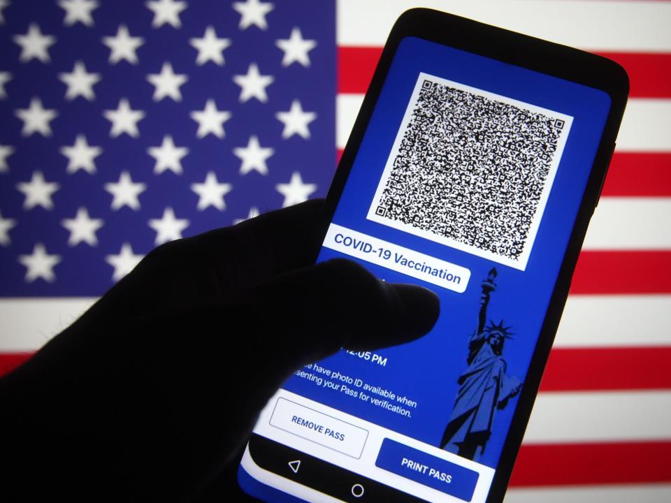 Excelsior Pass app which provides digital proof of COVID-19 vaccination or negative test results seen displayed on a smartphone screen in front of the US flag.