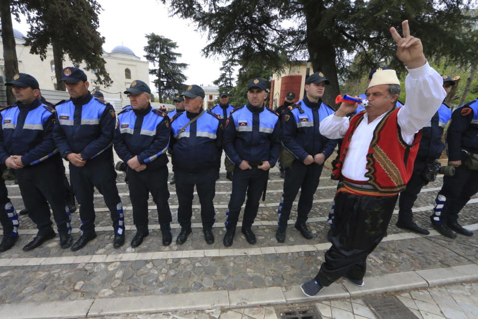 A protester dressed in traditional clothing flashes the victory sign in front of Albanian policemen guarding the parliament building in Tirana, on Thursday, March 28, 2019. Albanian opposition protesters have repeated attempts to enter the parliament by force in their protest asking for the government's resignation and an early election. (AP Photo/ Hektor Pustina)