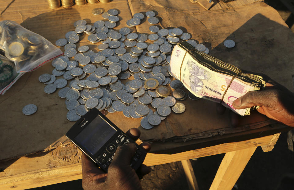 In this photo taken Thursday, Aug. 8, 2019, a vendor transacts on his mobile phone while selling cash in Harare Zimbabwe. With inflation soaring and cash in short supply, many Zimbabweans transfer funds using their mobile phones and pay a premium to get currency. (AP Photo/Tsvangirayi Mukwazhi)