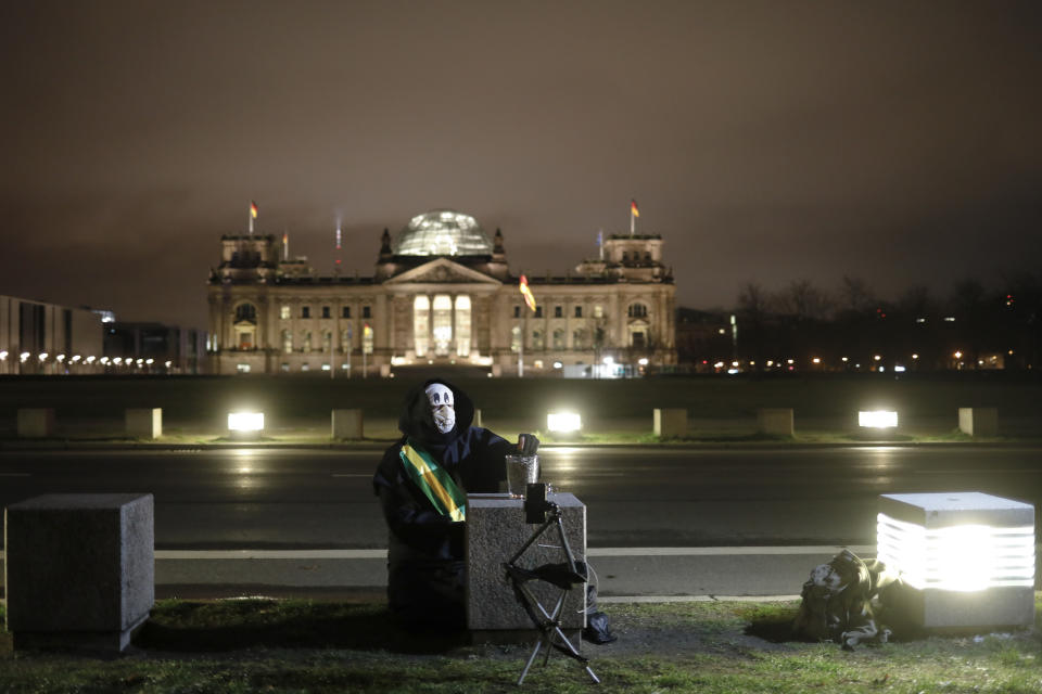 Brazilian activist and artist Rafael Puetter, dressed as the grim reaper, sits in front of the Reichstag building and counts sunflower seeds during a one-man protest through Berlin, Germany, early Wednesday, April 7, 2021. The multimedia artist starts his performance at the Brazilian embassy in Berlin at midnight every night to protest against Brazil's COVID-19 policies. Rafael Puetter walks to the Brandenburg Gate and then to the nearby German parliament building, in front of which he counts out a sunflower seed to represent each of the lives that were lost over the past 24 hours in Brazil because of the coronavirus pandemic. (AP Photo/Markus Schreiber)