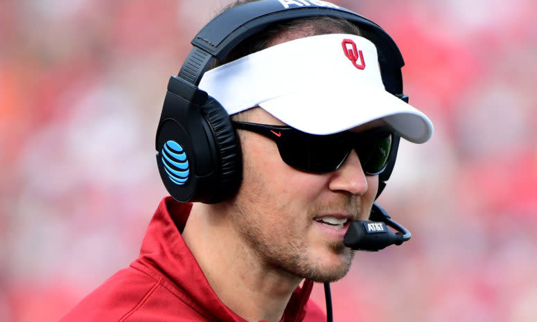 A closeup of Lincoln Riley wearing an Oklahoma Sooners visor and a headset.