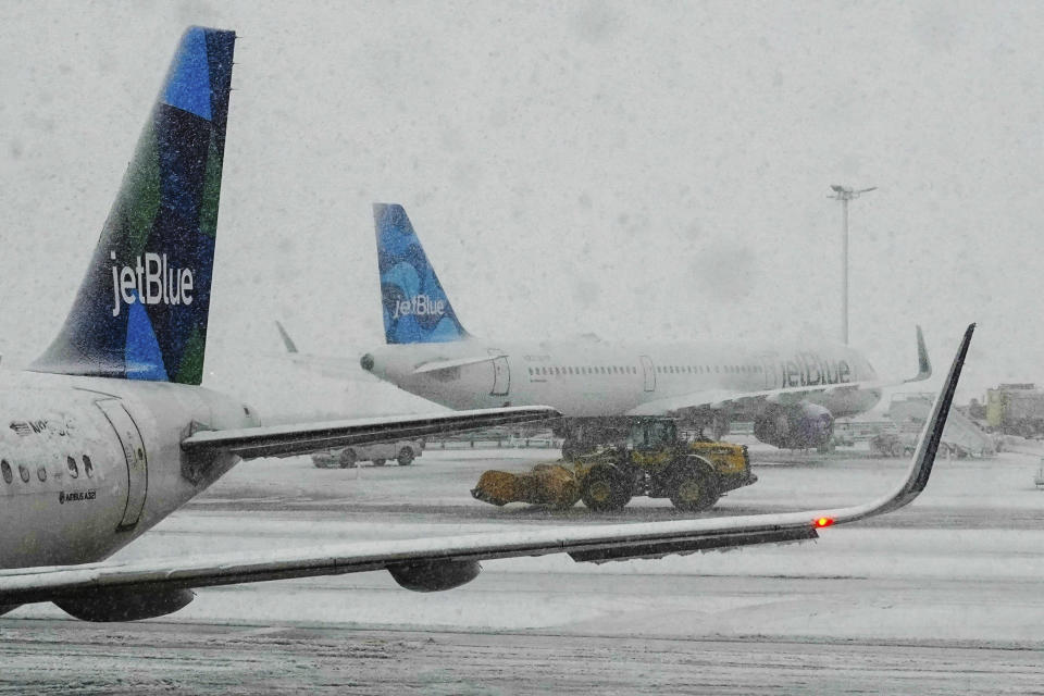 Workers clear the runway near JetBlue planes as snow falls at John F. Kennedy International Airport, Tuesday, Feb. 13, 2024, in New York. (AP Photo/Frank Franklin II)