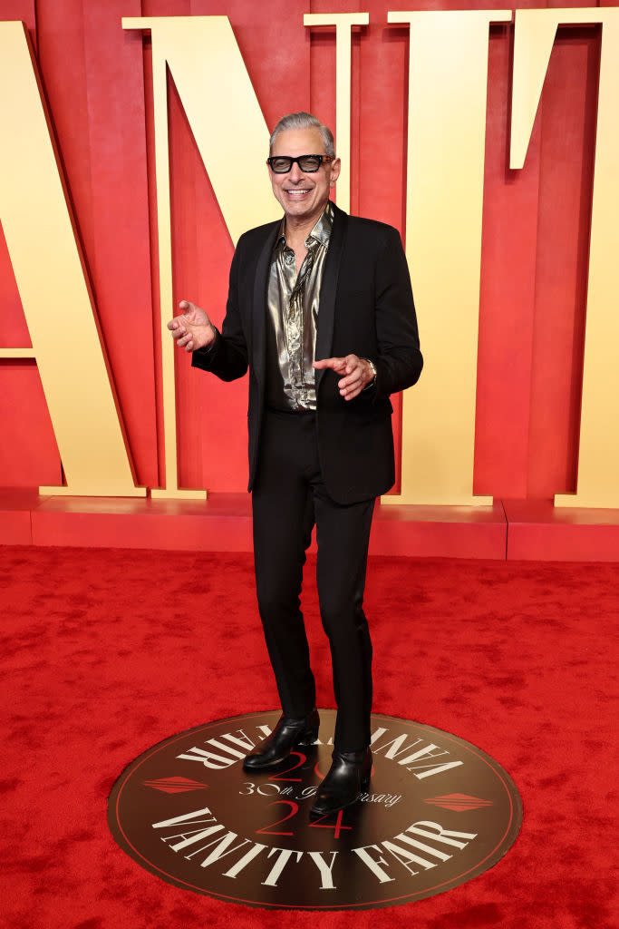 Jeff Goldblum in a black suit and patterned shirt, posing with a smile on the Vanity Fair Oscar Party red carpet