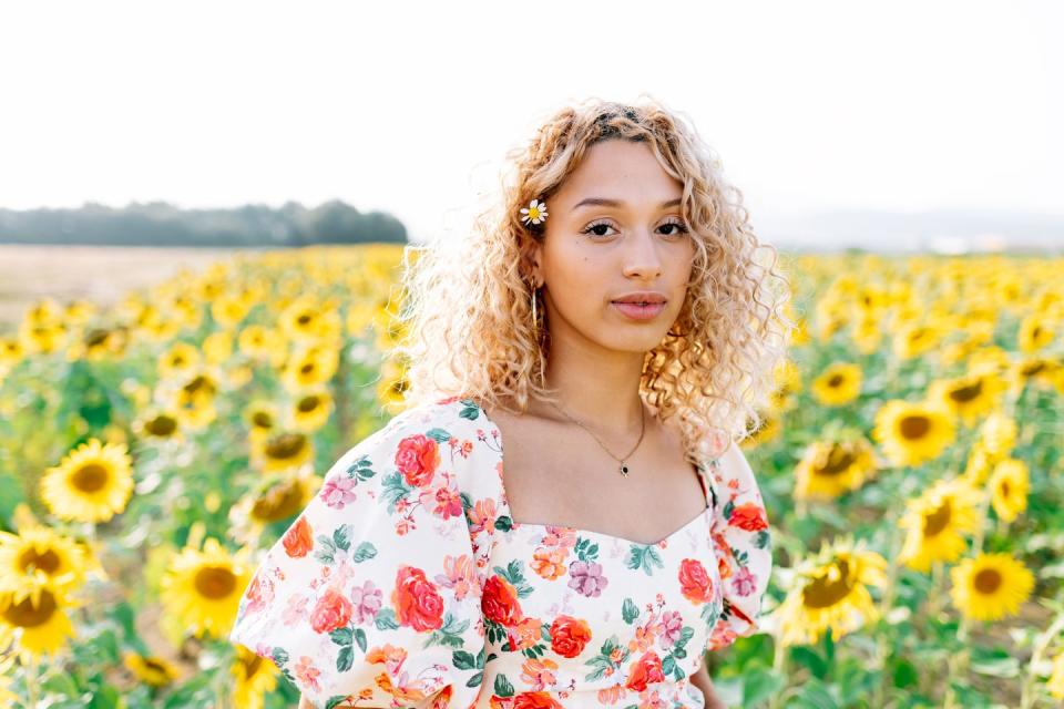 a young woman in a floral dress looking at the camera in a field of sunflowers