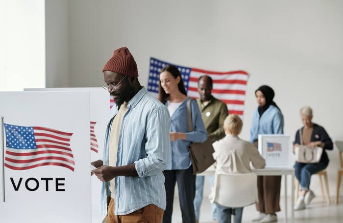 People at voting booths with "VOTE" signs and US flags, indicating a polling station
