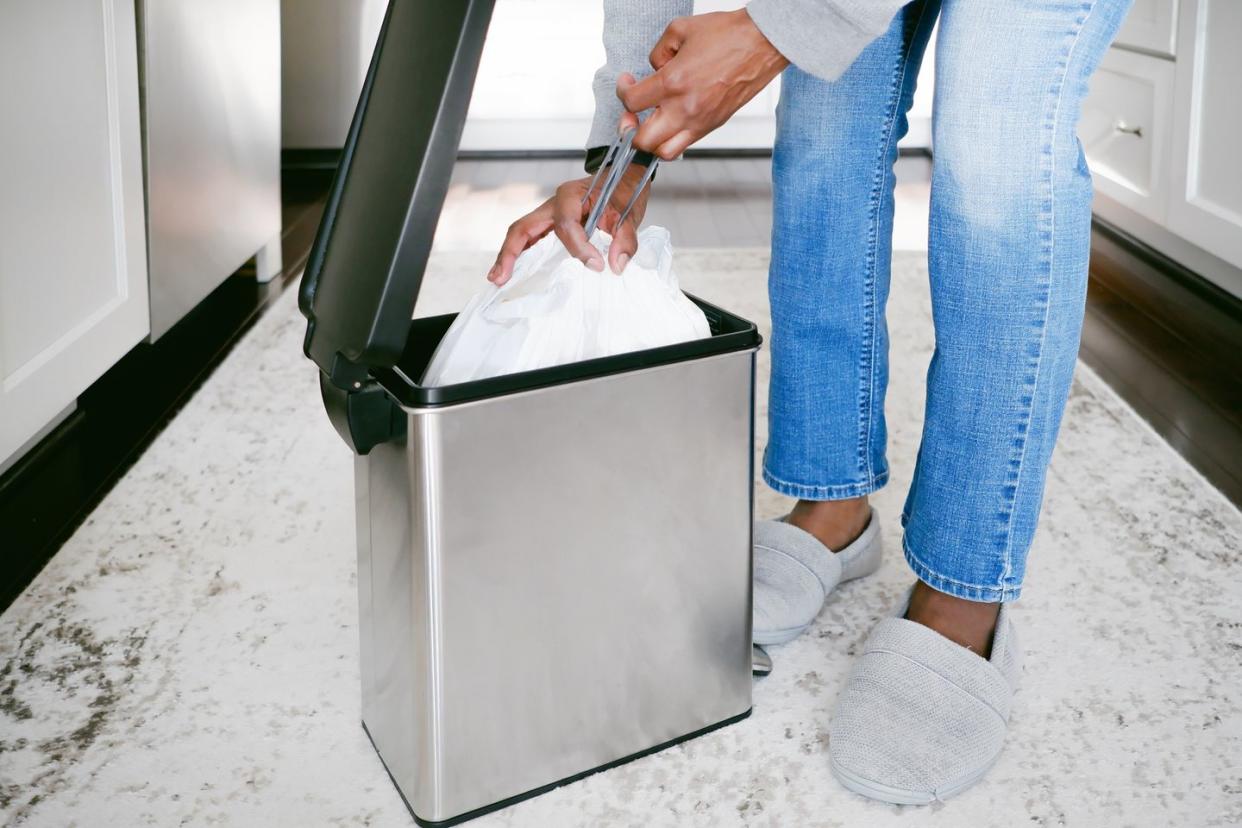 A woman takes out a garbage bag from a trash can