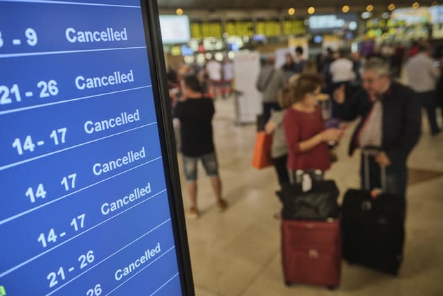 Passengers stand near a screen displaying cancelled flights