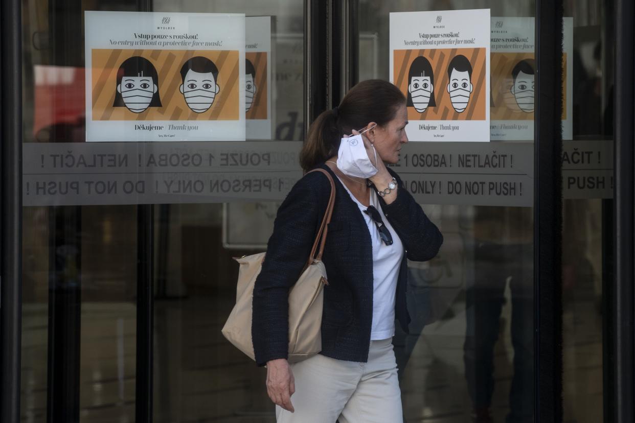 A woman takes off her face mask exiting a shopping mall in Prague as placards on the glass doors show masked faces, on Sept. 22, 2020. According to health ministry data, the Czech Republic registered a record high of 3,130 coronavirus cases on September 17, 2020, almost matching the total for the whole of March 2020.