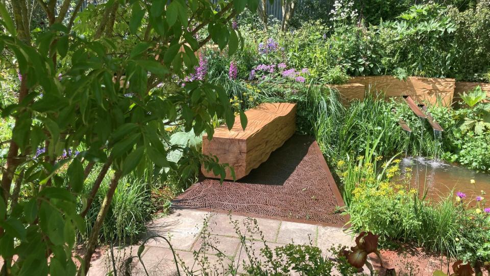 Large oak trees are used to create wooden benches to sit on overlooking a pond.