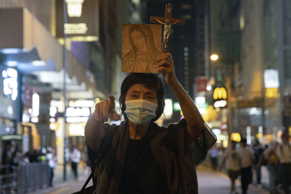 A woman offers prayer as policemen clear a road in Central in Hong Kong, Tuesday, Nov. 12, 2019. Police and protesters battled outside university campuses and several thousand demonstrators blocked roads as they took over a central business district at lunchtime on Tuesday in another day of protest in Hong Kong. (AP Photo/Ng Han Guan)