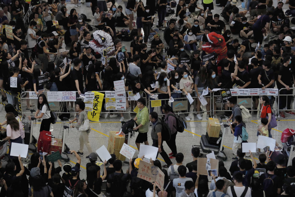 Passengers pass by thousands of protesters taking part in a second day of sit-in protest at the airport in Hong Kong on Saturday, Aug. 10, 2019. Hong Kong is in its ninth week of demonstrations that began in response to a proposed extradition law but have expanded to include other grievances and demands for more democratic freedoms. (AP Photo/Kin Cheung)