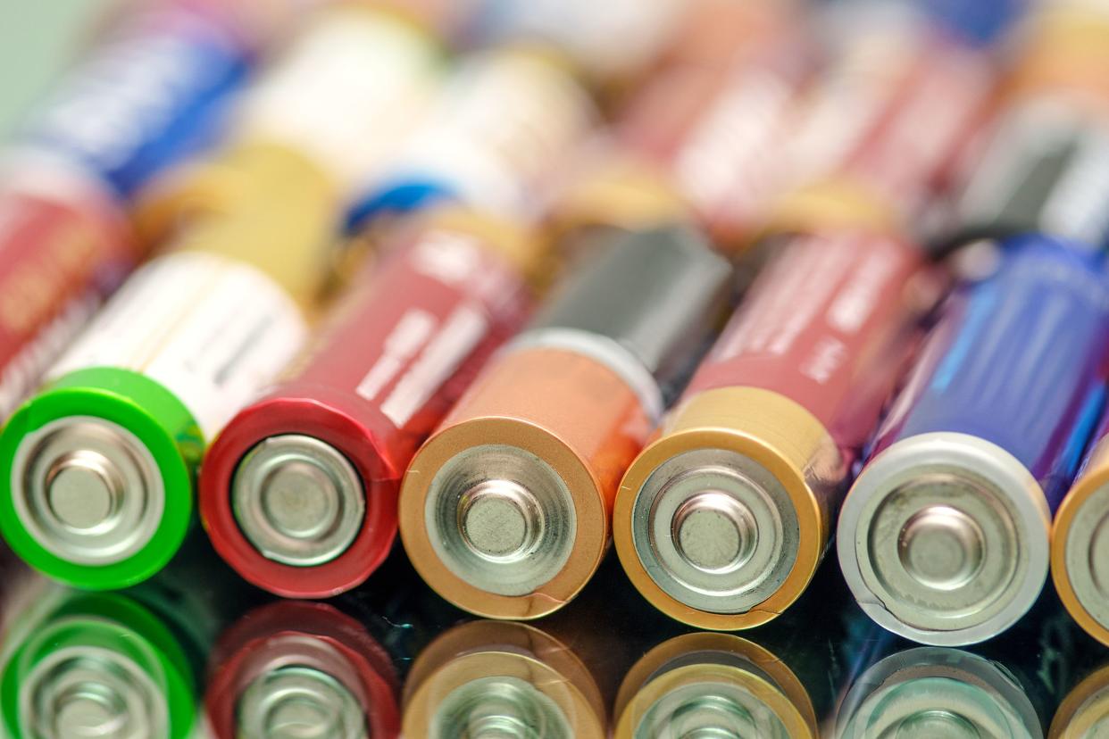 Closeup of a line of aa batteries, mixed assortment of brands, seven in closest line, reflected on a mirror, another line of batteries blurred behind it