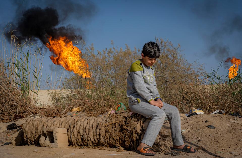 A young boy sits in front of the toxic chimneys of a gas flare in Nahran Omar, southern IraqBel Trew