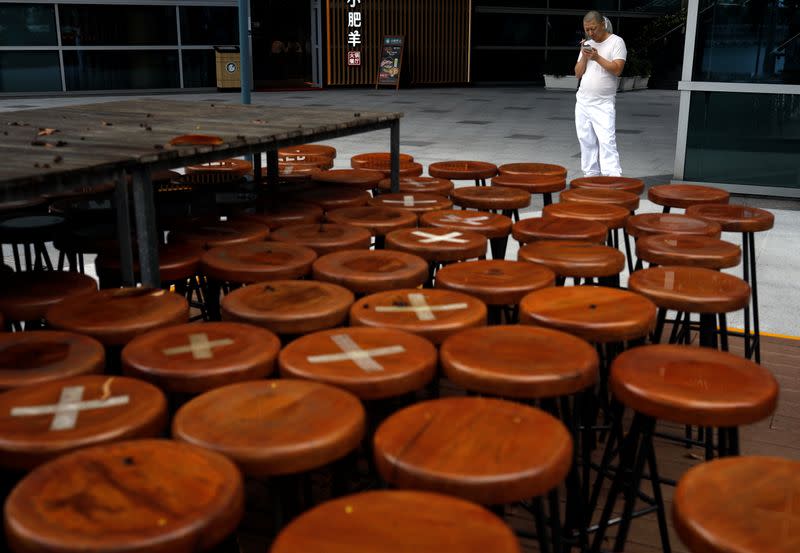 Kitchen assistant takes a break next to an outdoor seating area of a closed restaurant in Singapore