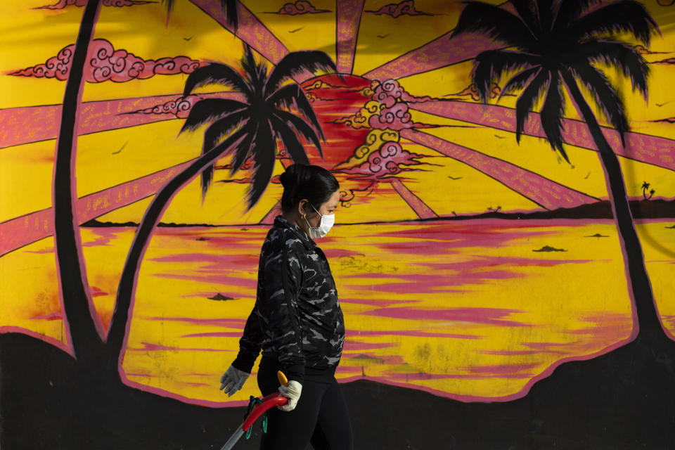 A woman walks past graffiti as she wears a protective face mask and gloves amid concerns over the country's coronavirus outbreak, in Tel Aviv, Israel, Monday, April 6, 2020. (AP Photo/Oded Balilty)